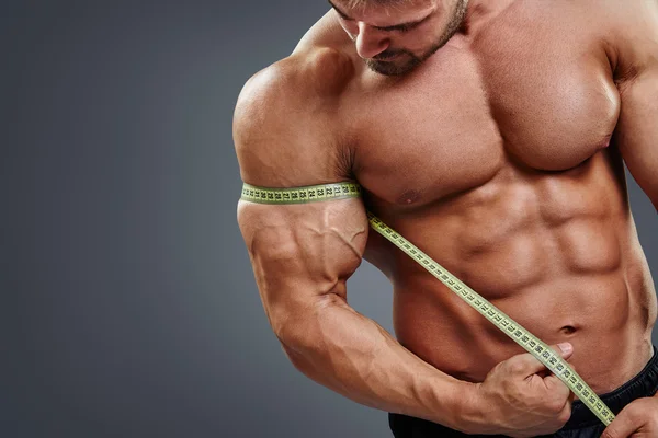 Bodybuilder measuring biceps with tape measure — Stockfoto