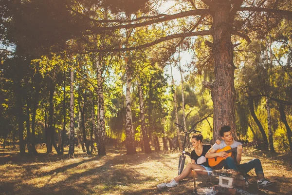 Girl and boy plays guitar outdoors by a tree — 图库照片