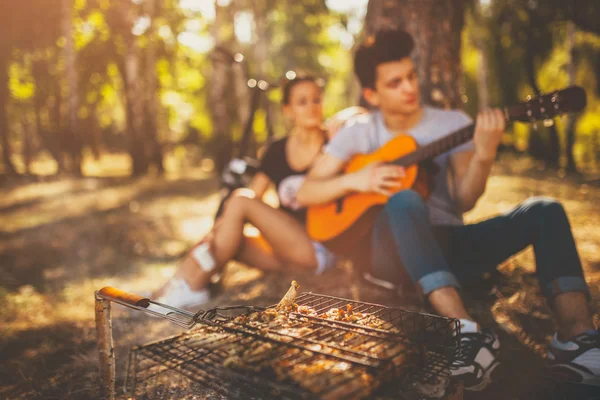 Piknik i grilla mięso. Młoda para gra na gitarze — Zdjęcie stockowe