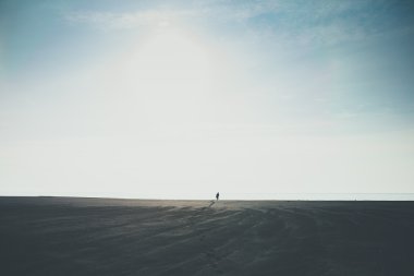 Ayak izleri bırakarak rahat İzlanda'daki siyah plajda ufka doğru yürüyen adam
