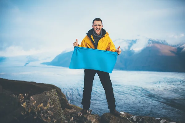 Joven sonriente sosteniendo una bandera en blanco en la cima de la montaña — Foto de Stock