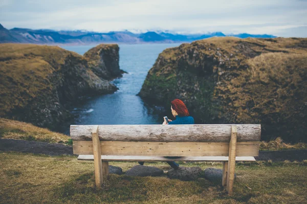 Bakifrån av kvinna sitter på en bänk och använder smartphone i Island — Stockfoto