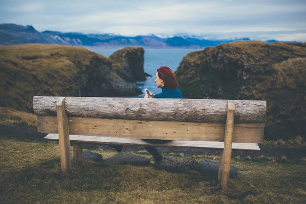 Bakifrån av kvinna sitter på en bänk och använder smartphone i Island. — Stockfoto