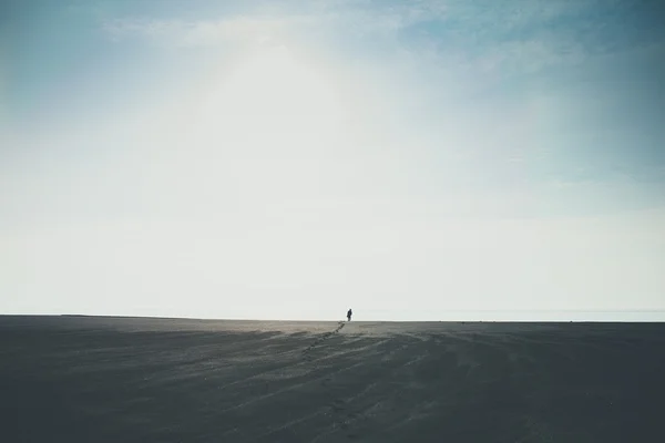 Man walking alone to horizon on black beach in Iceland leaving footprints Stock Photo