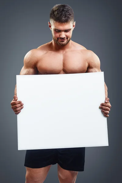 Gespierde bodybuilder man houden lege poster — Stockfoto