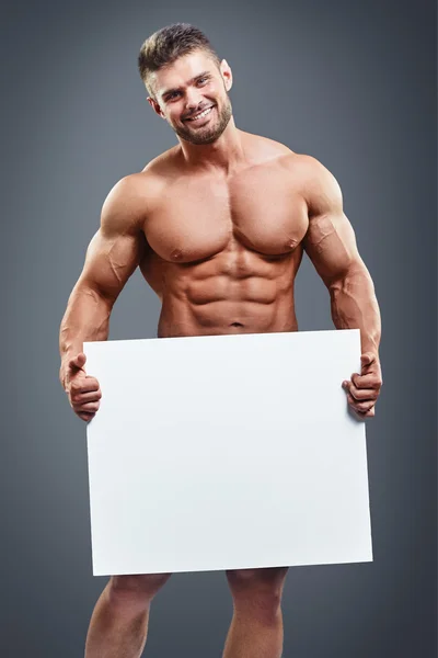 Muscoloso giovane uomo in possesso di poster bianco vuoto — Foto Stock