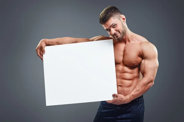 Fisiculturista segurando cartaz branco em branco — Fotografia de Stock