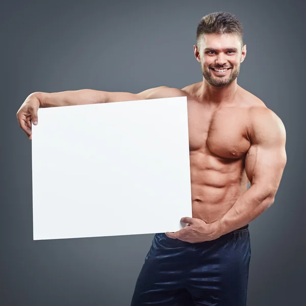 Construtor de corpo sorridente segurando cartaz branco em branco — Fotografia de Stock
