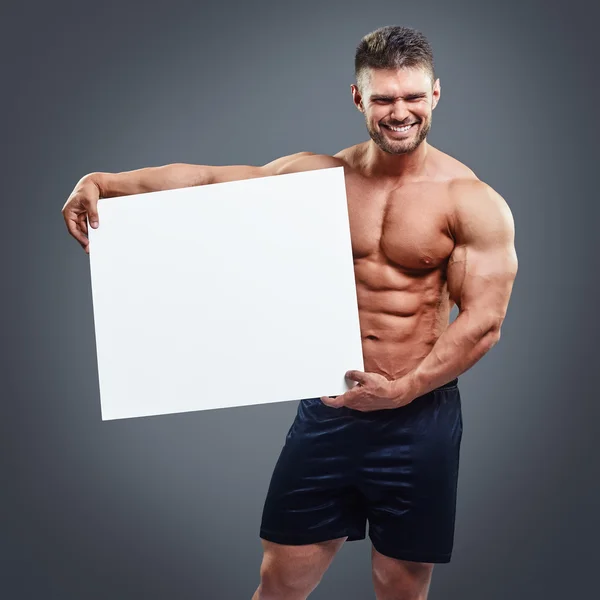 Muscular jovem segurando cartaz branco em branco — Fotografia de Stock