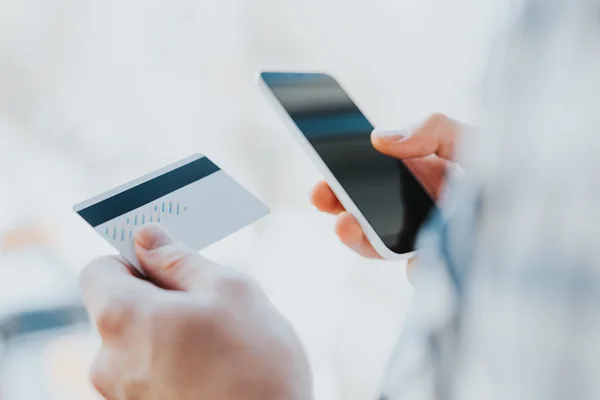Ung man händerna hålla kreditkort och använder telefon — Stockfoto