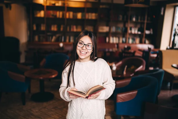 Dziewczyna student śmiejąc się i trzyma książkę w bibliotece — Zdjęcie stockowe