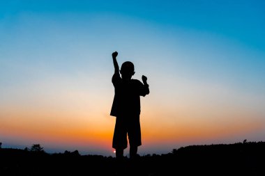 Siluet çocuk süper kahraman gibi elini kaldırıyor.