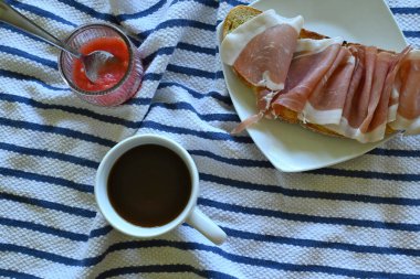 Mavi çizgili kumaş ve fotokopi uzayı üzerinde domates ve kahve ile hazırlanmış jambon tostlarının yatay genel çekimi.