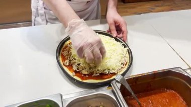Şef pizza hamuruna peynir ve sebze sürerek 4K 'lık görüntüyü kapatıyor. Temiz mutfak, fast food, italik yemek.