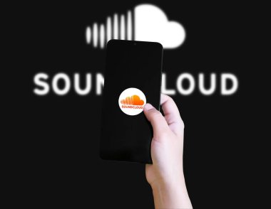 Elinde SoundCloud akıllı telefon uygulaması var. Arkaplanda bulanık logo var.