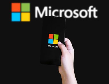 Microsoft logosunu bulanık arka plan illüstrasyon teknolojisi konseptiyle gösteren el ele tutuşan akıllı telefon