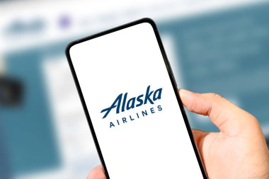 Close-up of hand holding smartphone with Alaska Airlines logo on screen illustrative editorial.