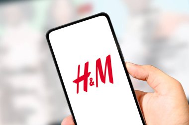 H & M logosu, çevrimiçi alışveriş ve moda perakendeciliği illüstrasyon konseptinde elde tutulan akıllı telefon ekranında gösterilir.