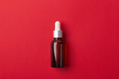 Kırmızı arka planda kehribar damlatan cam şişe. Model