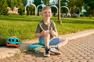 Beş yaşındaki küçük bir çocuk kaykaydan düştü, acı hissetti, bacağını yaraladı ve üzerine yara bandı yapıştırdı.