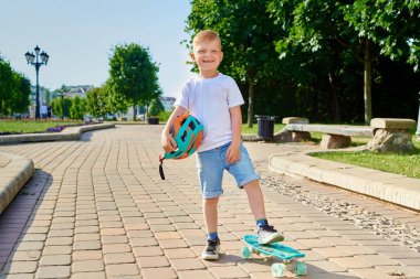 Küçük kızıl saçlı çocuk yazın parkta paten kaymayı öğreniyor.