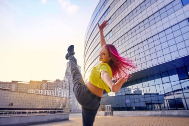 Parlak spor kıyafetleri ve boyalı pembe saçları olan genç bir kadın bacağını kaldırdı ve şehirde eğitim görüyor.