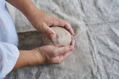 Yakın plan kadın elleri masadaki kilden bir parça yoğuruyor.