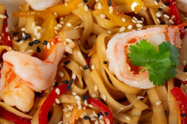 Kızarmış karides, kırmızı soğan ve dolma biberli Udon eriştesi kişniş ve susam tohumuyla süslenmiş. Geleneksel Asya mutfağı.