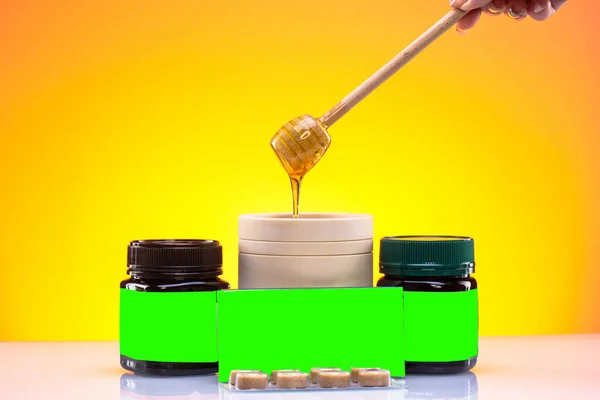 Honey drips into a wooden glass, on a yellow - orange background, next to a can of chromokey for inscriptions, for advertisements, billboards, billboards.