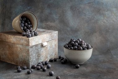 Blueberries in a cup, on a wooden table. The berries are scattered on the table. Blurred background. Rustic style. Healthy diet.