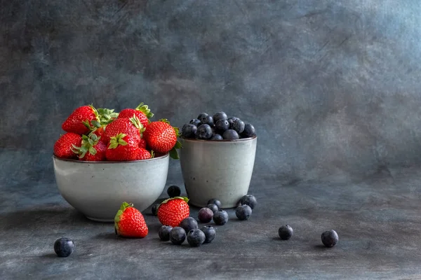 Strawberries and blueberries in a cup, on a wooden table. Blurred background. Rustic style. Healthy diet.