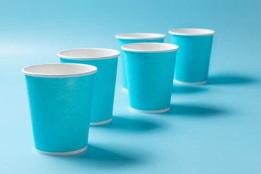 Açık mavi arka planda tek kullanımlık kağıt bardak. Tek kullanımlık sofra takımı. Kavram.