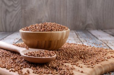 Dağınık karabuğday. Tahta bir kasede karabuğday ve kaşık tahta bir masanın üzerinde yatıyor. Dağınık karabuğday. Sağlıklı beslenme. Diyet yemek. Uzayı kopyala Yakın plan. Yüksek kalite fotoğraf