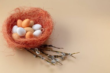 Easter colorful eggs in a basket and branches of pussy willow on a beige background. Colored eggs. Easter still life. Wooden background. Place for your text. High quality photo