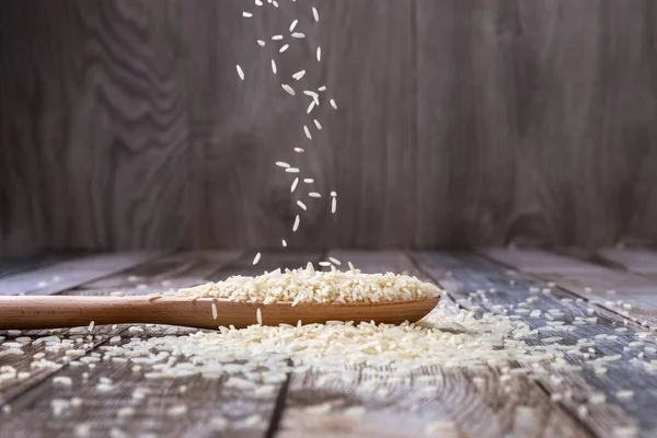 Çiğ pirinç ahşap bir kaşıktan masaya dökülür. Pirinç hokkaları masaya saçıldı. Havalanma. Sağlıklı beslenme. Diyet yemek. Yakın plan. Yüksek kalite fotoğraf