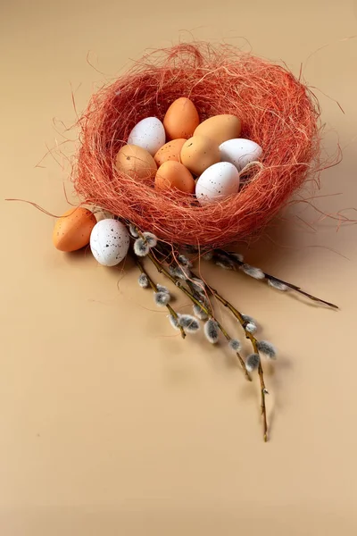 Easter colorful eggs in a basket and branches of pussy willow on a beige background. Colored eggs. Easter still life. Wooden background. Place for your text. High quality photo