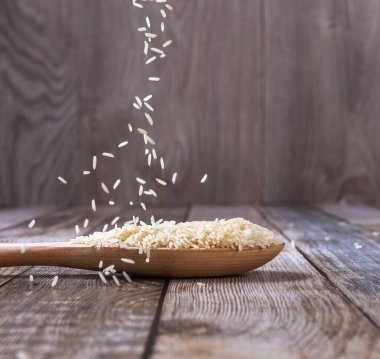 Çiğ pirinç ahşap bir kaşıktan masaya dökülür. Pirinç hokkaları masaya saçıldı. Havalanma. Sağlıklı beslenme. Diyet yemek. Yakın plan. Yüksek kalite fotoğraf