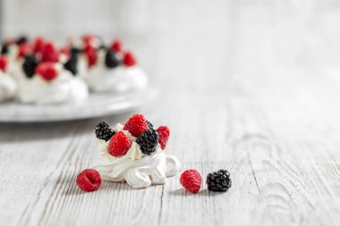 Pavlova 'nın keki açık ahşap bir masada. Kremalı pasta, ahududu ve böğürtlenli. Yüksek kalite fotoğraf