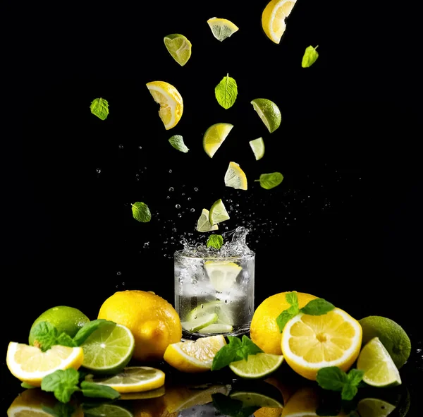 Citrus lemonade with ice in a glass decorated with lemon, lime and mint slices and on a black background. Splash. Detox. Healthy food rich in vitamins and antioxidants. Copy space. High quality photo