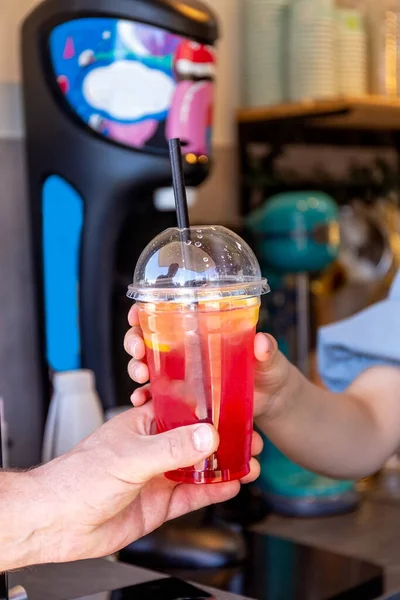 Plastik bardakta meyveli kokteyl. Alkolsüz portakal ve çilekli kokteyl. Elin bir bardak limonata tutuyor. Alıcı bir kokteyl aldı. Konsept götür. Yüksek kalite fotoğraf