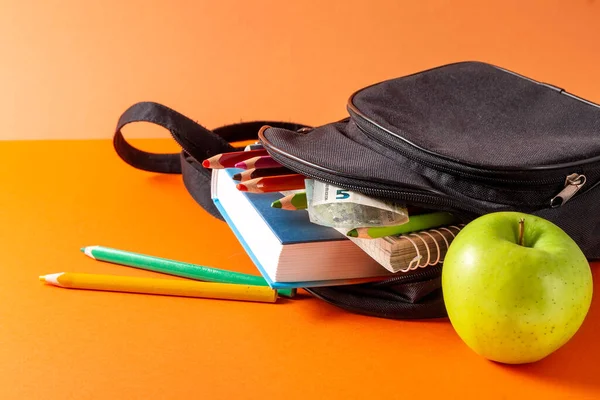 Open school backpack on an orange background. Books, a notebook and pencils are sticking out of an open school backpack. Education concept. High quality photo