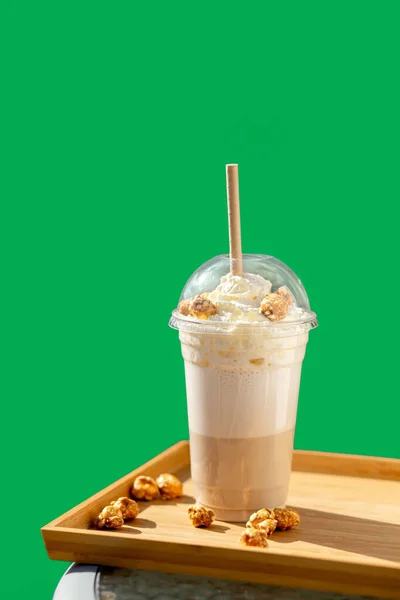 Frappe with whipped cream and popcorn flavoron a green background. Frappe in a plastic disposable cup with a lid. Take away. — Stock Photo, Image