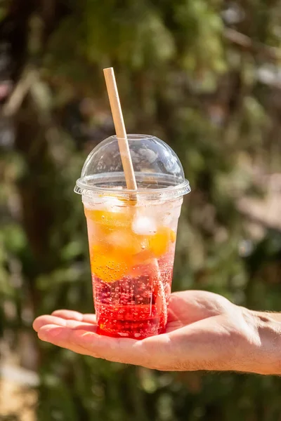 Fruitcocktail met ijs in een plastic glas. Zomer drankje. Een glas limonade in de hand. Concept meeneem. — Stockfoto