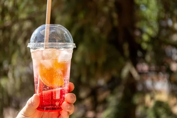 Κοκτέιλ φρούτων με πάγο σε πλαστικό ποτήρι. Θερινό ποτό. Ένα ποτήρι λεμονάδα στο χέρι. Αντίληψη παίρνει μακριά. — Φωτογραφία Αρχείου