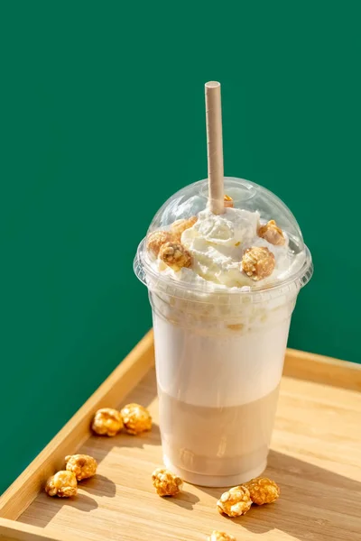 Frappe met slagroom en popcorn smaak op een groene achtergrond. Frappe in een plastic wegwerpbeker met deksel. Neem weg.. — Stockfoto