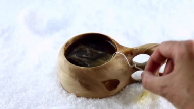 Kuksa. Fin ahşap bardağında çay. Geleneksel Finlandiya ahşap bardağı karda. Kaynar su jeti. El fincandan bir poşet çay çıkarır..