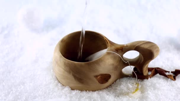 Kuksa. Een thee in een Finse houten beker. Traditionele Finse houten beker in de sneeuw. Een kokende waterstraal. De hand stopt de theezakje in de beker. — Stockvideo