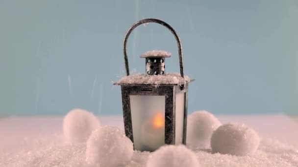 A candle is burning in a candlestick. Candlestick and snowballs of snacks in the snow. Snowing. Christmas mood. — Stock Video