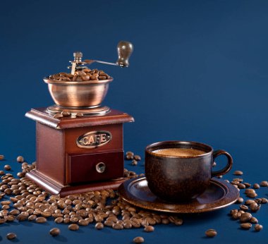 Kahve fincanı ve kahve değirmeni ile mavi arka planda kahve çekirdekleri..