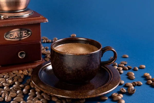 Copo com café e moedor de café manual com grãos de café em um fundo azul. — Fotografia de Stock